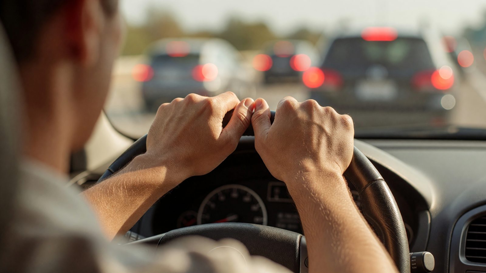 Mains sur un volant de voiture, à l'arrêt dans un bouchon sur l'autoroute en pleine journée