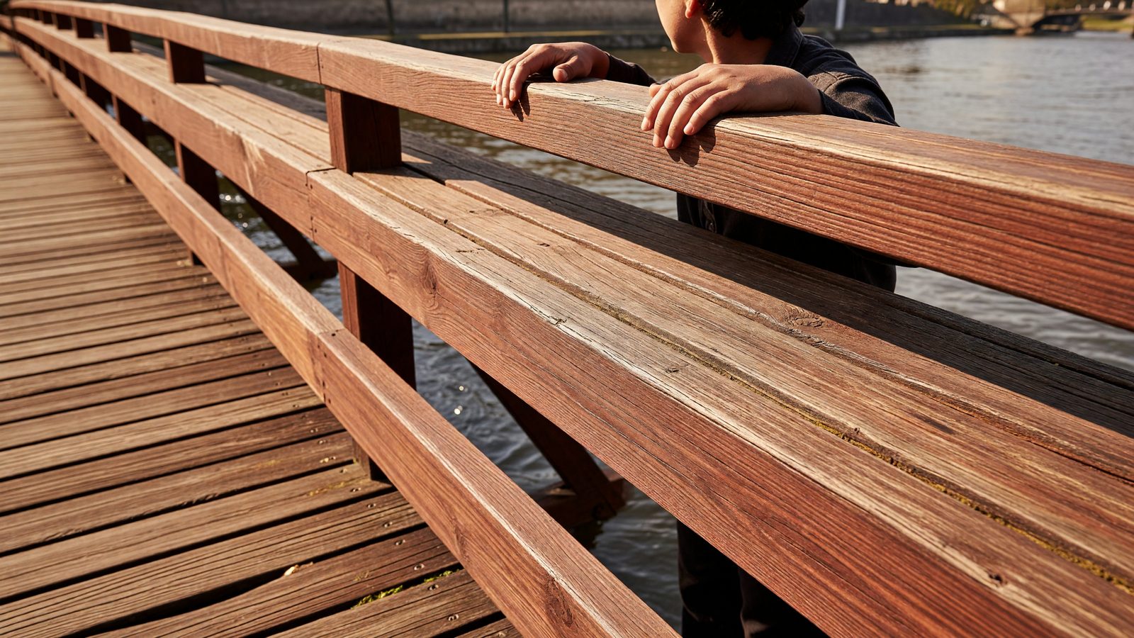 Détail d'une main posée sur la rambarde en bois de la passerelle, au-dessus de la Moselle à Metz